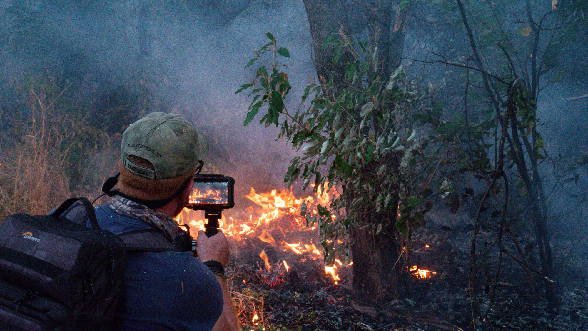 Cameraman filming a controlled burn at dusk in Australian bushland